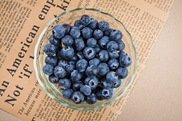 Blueberry fruit in glass cup on newspaper and wood table background