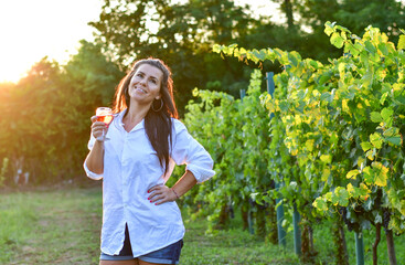 Fototapeta premium Young beautiful Happy smiling Brunette Woman posing at Vineyard with a glass of rose wine.Wine tourism