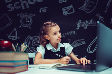 beautiful pupil sitting at desk and study online with laptop against black background