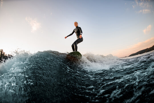 athletic woman wakesurfing on the board down the river against the background of blue sky