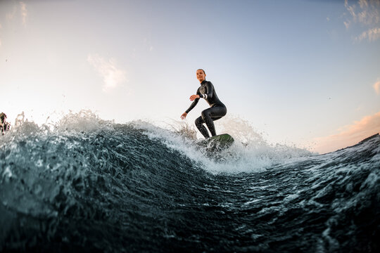 athletic female wakesurfer on the board rides down the river wave against the background of blue sky