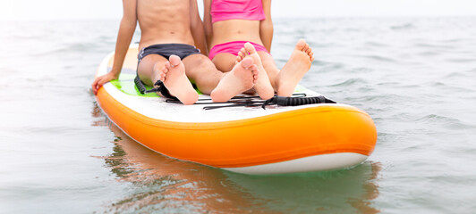 Two persons, boy and girl, sitting on the paddle board on the calm sea surface. SUP boarding, water sports. Active healthy lifestyle. Wide Travel banner.