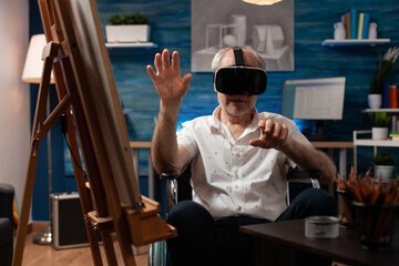 Invalid aged artist using vr glasses to draw masterpiece design on canvas and easel at fine art studio. Disabled senior man with modern headset sitting in wheelchair, for drawing hobby