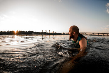 Fototapeta na wymiar view of adult man in swimming vest swims in the water leaning on wakeboard