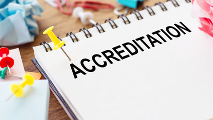 ACCREDITATION - text on a notepad with wrinkled paper and paper needles on wooden background.