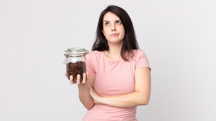 pretty woman shrugging, feeling confused and uncertain and holding a coffee beans bottle