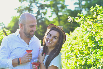 Portrait of a smiling happy couple kissing in a Vineyard toasting wine. Beautiful brunette woman and bearded muscular man spending time together