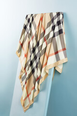 Subject photo of bright scarf with checked Scottish design. Stylish silk headkerchief is hanging on the white board.  