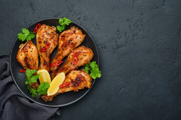 Grilled chicken drumsticks or legs or roasted bbq with spices and tomato salsa sauce on a black plate. Top view with copy space.