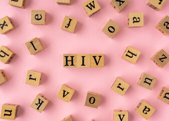 HIV word on wooden block. Flat lay view on light pink background.