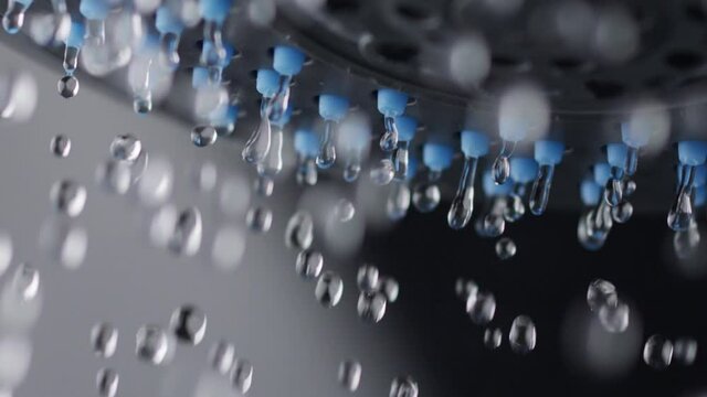 Water drops slowly fall down from the shower head. Slow motion shot of shower water. Macro shot, black background