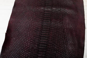 Brown burgundy dyed folded natural genuine python leather on the wooden table	
