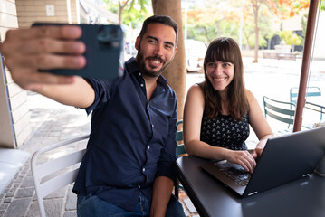 colleagues taking a selfie while working with the laptop on the terrace of a cafeteria
