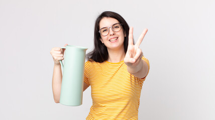 pretty woman smiling and looking happy, gesturing victory or peace and holding a coffee thermos © kues1