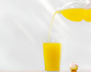 Orange drink being poured into a glass on a light background.