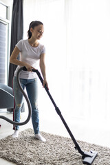 Cleaning concept. Young woman cleaning carpet with vacuum cleaner at home