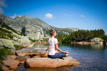 healthy young woman doing yoga in mountain landscape by lake