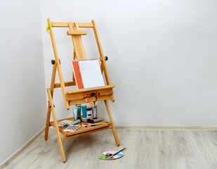 An easel with sketchbooks and paints stands in the corner of the beige room.