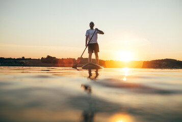 Man paddleboarding on the lake at sunset - obrazy, fototapety, plakaty