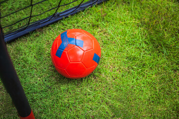 Soccer goal and a red soccer ball for kids practicing on the green.