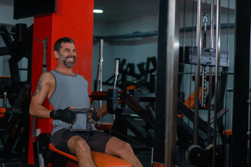 Fototapeta na wymiar Fitness training in sport gym of active male with beard sitting and pulling heavy weight on exercise equipment