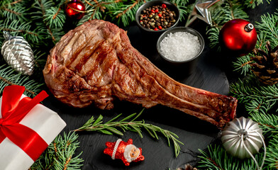 Grilled Christmas tomahawk steak with fir tree and tree decorations on stone background