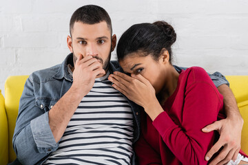 Frightened interracial couple looking at camera at home