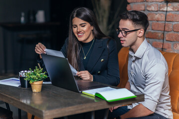 Business meeting inside a cafe with two young colleagues sitting at a table, sharing some new ideas and looking at their laptops