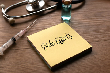 A bottle of vaccine, syringe, stethoscope and yellow memo note written with Side Effects on wooden background.