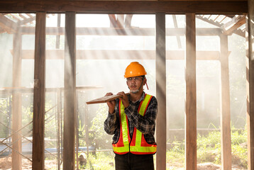 Asian young professional carpenter with wooden planks and tools stand in his wooden workshop as workers work in the background of an old wooden house