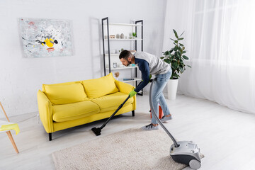 Side view of man cleaning floor with vacuum cleaner at home