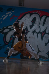 Fototapeta na wymiar Young black male dancing hip hop style in an urban setting. he is wearing a orange outfit and is on a graffiti background.