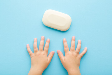 Baby boy hands and white natural soap on light blue table background. Pastel color. Closeup. Point of view shot. Care about clean and soft body skin. Daily children hygiene. Top down view.