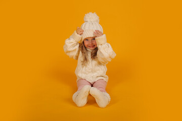 beautiful little blonde girl in a winter knitted white hat sweater and socks new year on a yellow background