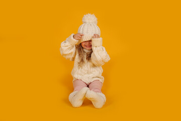 beautiful little blonde girl in a winter knitted white hat sweater and socks new year on a yellow background