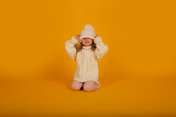 beautiful little blonde girl in a winter knitted white hat sweater and socks new year on a yellow background