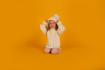 beautiful little blonde girl in a winter knitted white hat sweater and socks new year on a yellow background