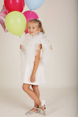 beautiful blonde girl in a white dress with wings with balloons in her hands holiday birthday