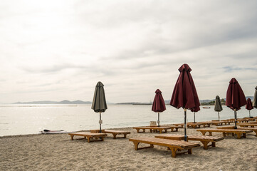 Naklejka premium Empty wooden deck beds and folded umbrellas on sand near Aegean Sea. Lounge chill zone on city beach in Athens, Greece