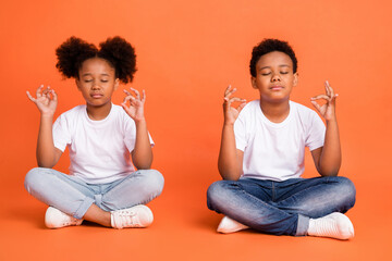 Full length photo of small rest girl boy sit closed eyes wear white t-shirt jeans sneakers isolated on orange background