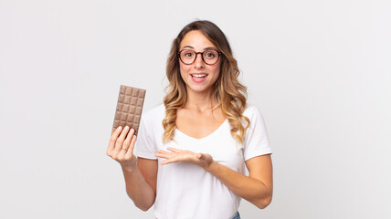 pretty thin woman smiling cheerfully, feeling happy and showing a concept and holding a chocolate bar - obrazy, fototapety, plakaty