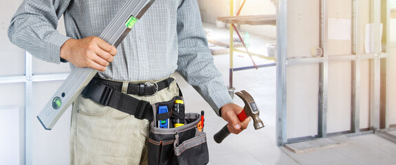 Fototapeta na wymiar Builder holds level and hammer against background of building walls under construction, hands with tools on main