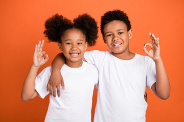 Photo of little funny girl boy hug show okey wear white t-shirt isolated on orange color background