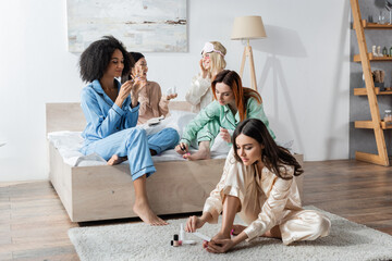 cheerful interracial women doing beauty procedures during slumber party