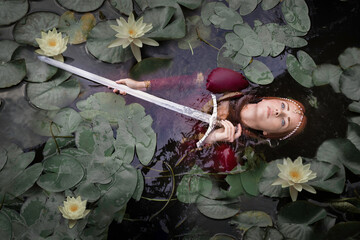 The mistress of the lake among the leaves of water lilies lies on the water with a sword