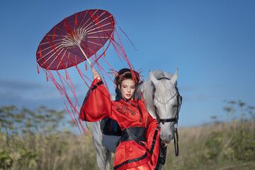 Girl in a red kimono under an umbrella with ribbons with a white horse