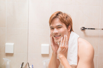 Man washing face with facial cleanser face wash soap in bathroom sink at home.