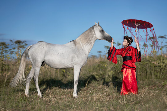 Girl in a red kimono with a white free horse in the field