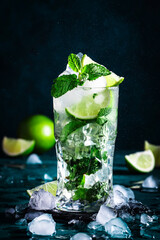 Mojito cocktail with lime, white rum, soda, cane sugar, mint, and ice in glass on deep blue background. Negative space
