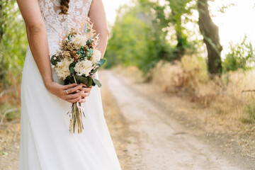 Girl dressed as a bride with a bouquet of preserved flowers between her hands on an out of focus...